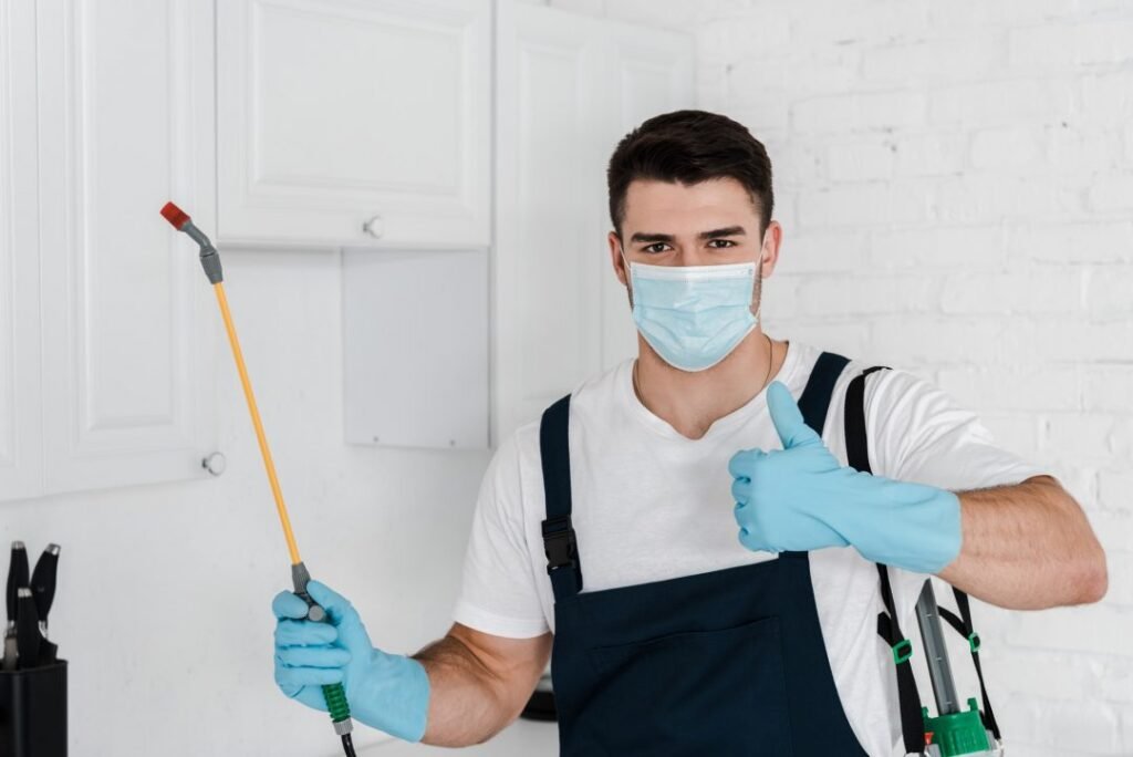 Exterminator in uniform holding toxic spray and showing thumb up.jpg